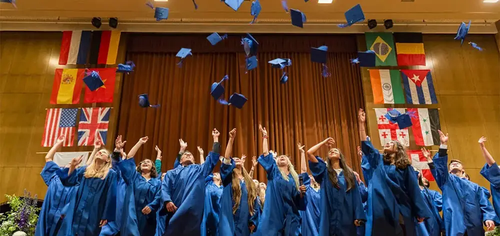 A group of people wearing blue graduation gowns throwing their caps in the air